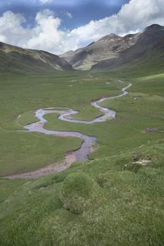 Winding river flowing through green mountain valley landscape Stock Photos
