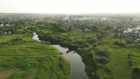 Winding river flowing through misty countryside, revealing peaceful small town Stock Footage 318312334