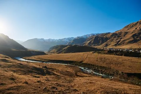 A winding river flows in a valley between high autumn mountains on a sunny clear Stock Photos