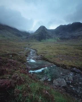 A winding river leading to cloud-covered mountain peaks Stock Photos