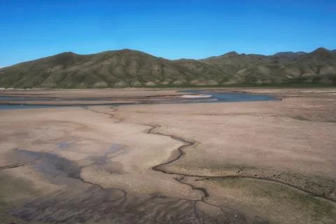 A winding river stream flowing through a dry textured sand valley with green  Stock Photos
