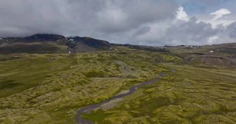 Winding River Through Mossy Lava Fields, Mountains Clouds, Aerial View Stock Footage 335078643