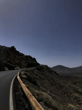 A winding road meanders through rugged mountains under a clear blue sky, show Stock Photos