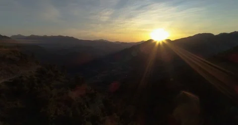 Winding road on mountain side lit by sunrise over mountains drone aerial 4k Stock Footage 125754405
