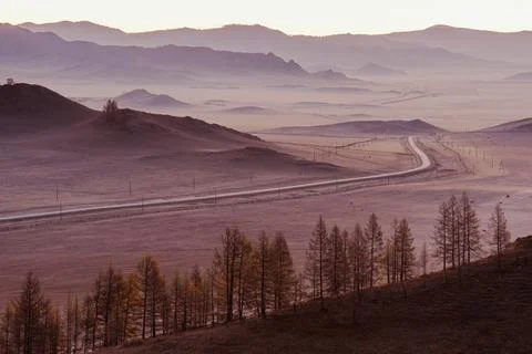 Winding road passes by fields and hills, beautiful foggy sunrise in steppe Stock Photos