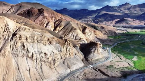 Winding Road Through Arid Mountains and Green Valley Under Cloudy Sky Tibet 動画素材 346738062