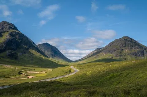 Winding road through a dramatic glen flanked by steep Highland peaks as see.. Stock Photos