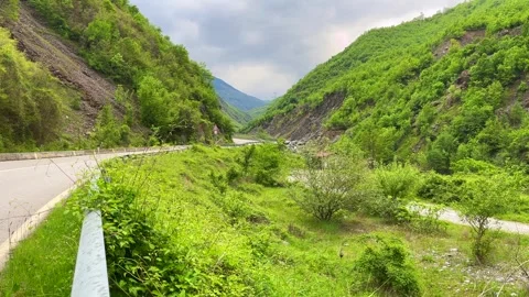 Winding road through green valley and mountains under cloudy sky Stock Footage 310246716
