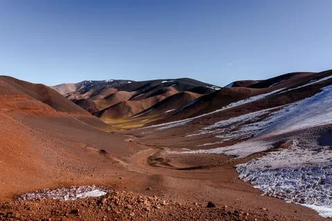 Winding road through red mountain valley with snow patches Stock Photos