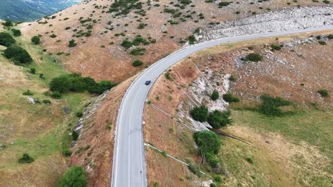 Winding Road Through Vibrant Green Hills at Sunset With a Solitary Car Passing 스톡 동영상 281289088