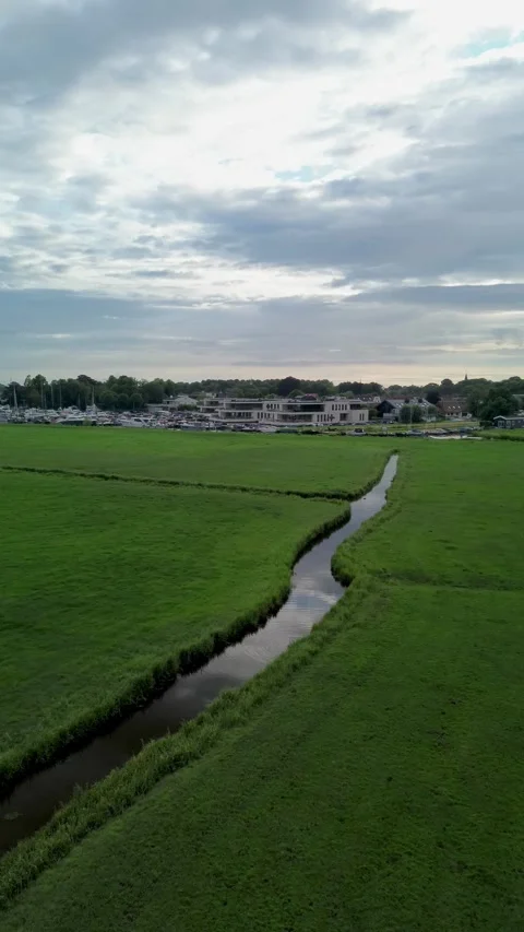 A winding stream flows through lush green meadows, reflecting the cloudy sky 스톡 동영상 316551209