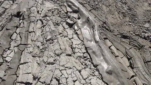 Winding stream of wet gray mud flowing across dry cracked desert earth Stock Footage 339270037