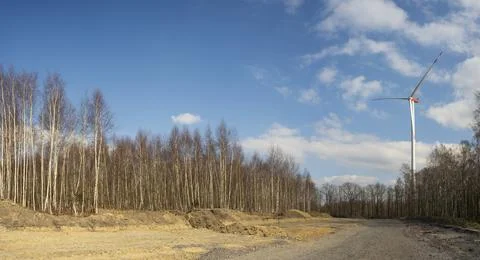A windmill with a blue sky and clouds. A dirt road with trees in the backgrou Foto stock