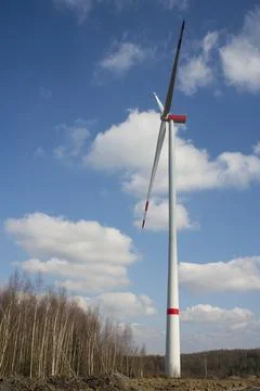 A windmill with a blue sky and clouds. A dirt road with trees in the backgrou Stock Photos