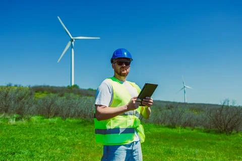 Windmill engineer checks data on tablet while standing in green field under.. Stock Photos