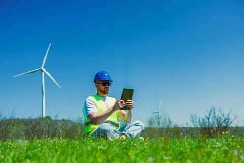 Windmill engineer checks data on tablet while sitting on grass near wind tu.. Stock Photos