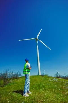 A windmill engineer observes a large wind turbine standing on a green hill. T Foto stock