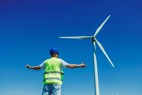 Windmill engineer in safety gear stands with arms outstretched near a wind tu Stock Photos