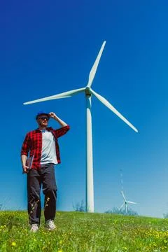 Windmill engineer standing near large turbine in open field under clear blu.. 写真素材