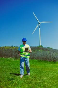 A windmill engineer stands in a green field with a wind turbine in the backgr Foto stock
