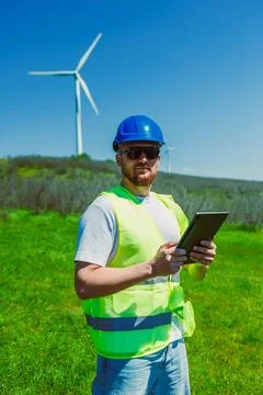 Windmill engineer stands in a green field with wind turbines in the backgroun Foto stock