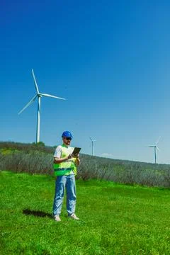 Windmill engineer stands in a green field looking at a device in hand. Large  Stock Photos