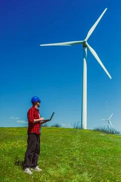 A windmill engineer stands in a green field with a laptop. The engineer looks Foto stock