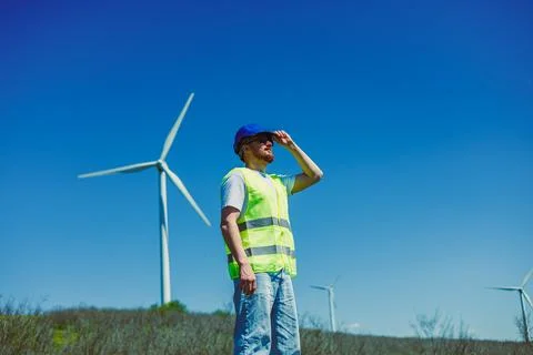 A windmill engineer stands in an open field. He wears a safety vest and a cap 写真素材