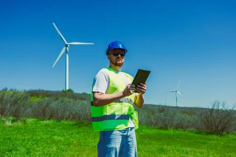 Windmill engineer uses a tablet to review information while standing on green Stock Photos