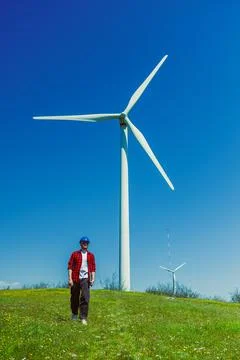 Windmill engineer walks near wind turbine in sunny weather on green hill in.. Stock Photos