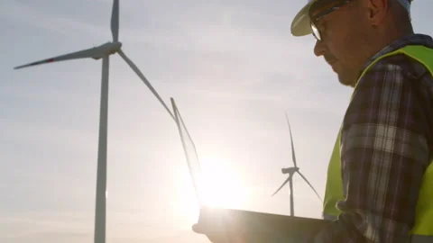 Windmill engineer watching wind turbines in operation on a laptop Stock Footage 192847349