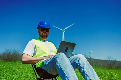 Windmill engineer working on a laptop in an open field under a clear sky ne.. Stock Photos