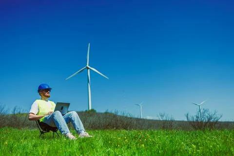Windmill engineer working on a laptop outdoors while seated on a chair in a.. Foto stock
