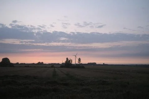 A windmill is in the middle of a field with a beautiful sunset in the backg.. Stock Photos