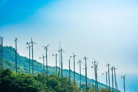 Windmill park on the background of blue sky, green mountains and the sea in the Stock Photos