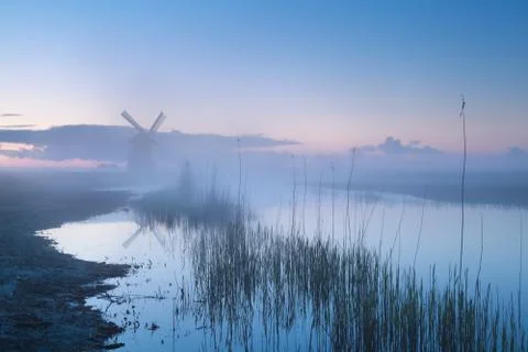 Windmill by river in misty dusk Stock Photos