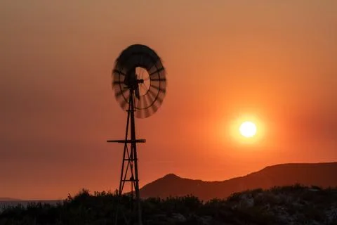 Windmill spinning in the wind at sunset with orange red sky and yellow sun Stock Photos