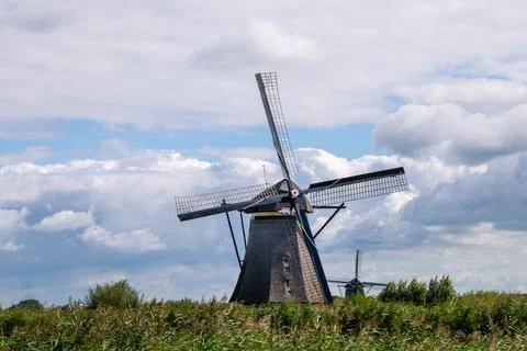 A windmill is standing in a field with a cloudy sky in the background Stock Photos