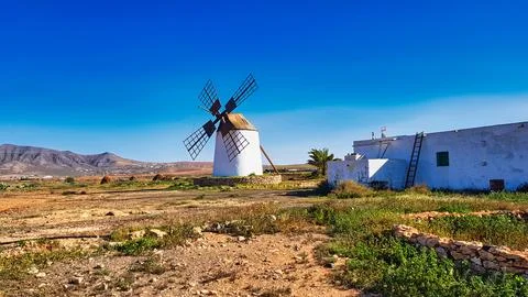 Windmill stands in a field with mountains in the background on a clear day Stock Photos