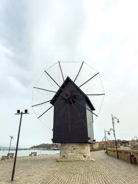 Windmill stands on the waterfront path near the coast during a cloudy day, .. Stock Photos