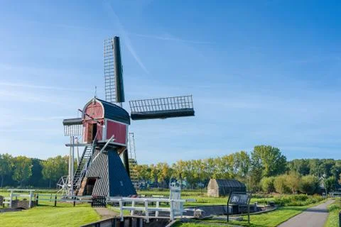 Windmill surrounded by green trees and vegetation under a clear blue sky Stock Photos