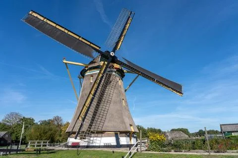 Windmill surrounded by green trees and vegetation under a clear blue sky Stock Photos