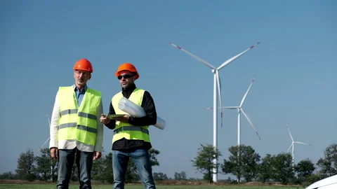 Windmills generate energy behind engineers on foreground Vidéo 164376470