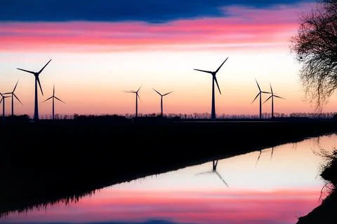 Windmills lining a river at sunset, enhancing the natural landscape Stock Photos