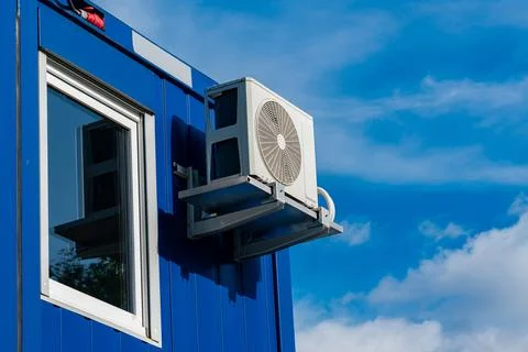 Window air conditioning unit mounted on blue building Stock Photos
