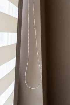 Window blind cord hanging in loop against neutral taupe wall beside layered Stock-Fotos