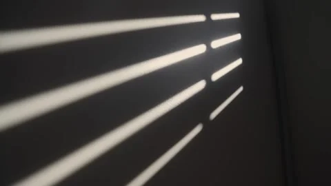 Window blind shadows opening on wall creating abstract light patterns Vídeo Stock 316069003