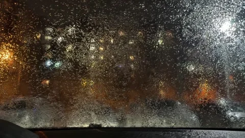A window of a car is covered in rain and the street lights are on Stock Footage 276719927