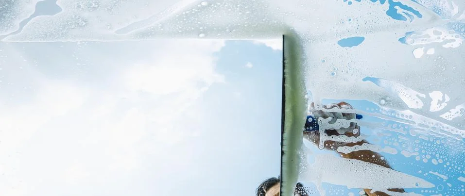 Window cleaner cleaning window with squeegee and wiper on a sunny day Stock Photos