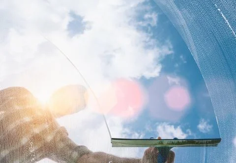 Window cleaner cleaning window with squeegee and wiper on a sunny day Stock Photos